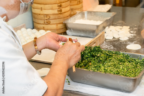 Фотография In a semi-open kitchen, chefs carefully prepare xiaolongbao by flattening dough into thin wrappers and filling them with minced pork and chives