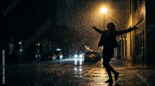 A silhouette of a person joyfully dancing in the rain on a dimly lit street at night, with wet pavement reflecting the streetlights.