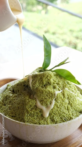 Cinematic action shot of pouring sweet condensed milk from a pitcher over fluffy matcha green tea shaved ice (Bingsu), mouth-watering summer dessert