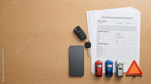 Car keys and insurance documents on wooden desk with smartphone and toy cars