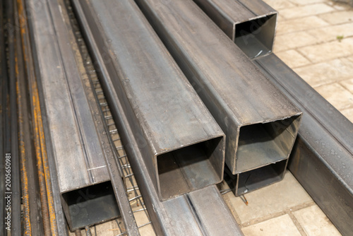 Stack of rectangular steel pipes and metal profiles lying on paving stones outdoors. Industrial material photography. Construction and metalworking industry concept. Design for banner, poster.
