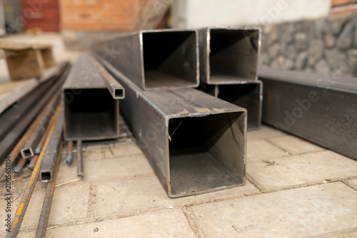 Stack of rectangular steel pipes and metal profiles lying on paving stones outdoors. Industrial material photography. Construction and metalworking industry concept. Design for banner, poster.