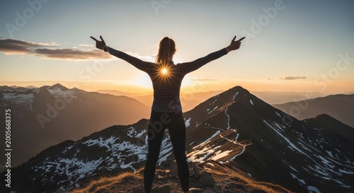 woman standing on mountain peak with arms outstretched at sunset