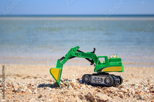 Toy excavator on sandy beach near the sea. Summer vacation, childhood play, beach toys and family holiday concept.