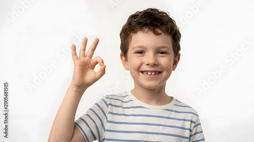 A happy young boy with curly brown hair, wearing a striped t-shirt, gives an OK gesture, symbolizing approval and success