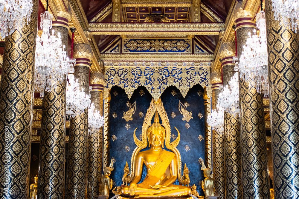 Obraz premium Golden Phra Phuttha Chinnarat Buddha statue in the ornate chapel of Wat Phra Si Rattana Mahathat with crystal chandeliers and golden pillars