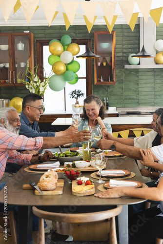 Host raising glass initiating toast, group clinking glasses, passing bread and sharing food