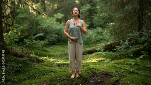 Woman placing hand on chest in mossy forest clearing