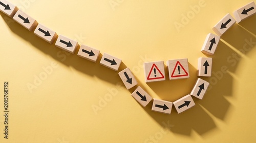 Wooden blocks with arrow icons changing direction to avoid red warning symbol on yellow background. Concept of business strategy, decision making, and problem solving.