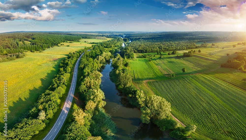 Naklejka premium scenic country road winds through landscape under a summer sky surrounded by green fields and trees beautiful drone aerial view landscape of green nature cultivated agricultural farm and river