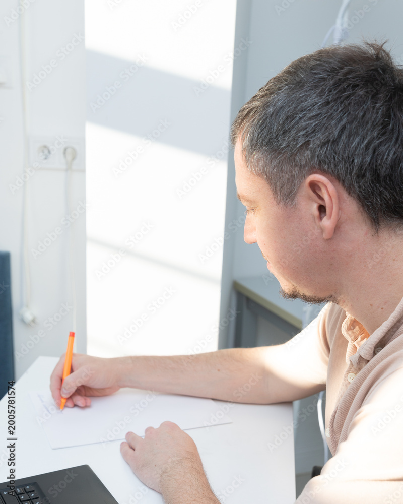 Fototapeta premium A man works at his desk at home, in a home office, writing, signing, and stamping his name