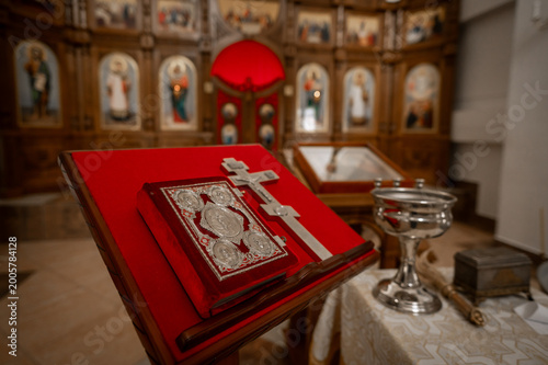 Foto Orthodox Gospel book and silver cross on red velvet lectern in church with icono
