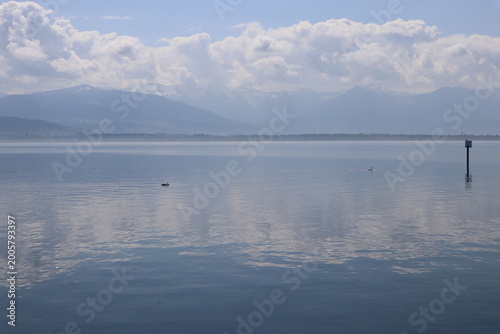 Fotografie Wide serene panoramic view of a calm misty alpine lake with mirror-like water su