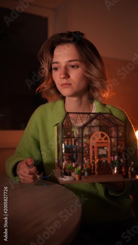 Young woman meticulously assembling a detailed miniature DIY greenhouse kit by hand. Focus on her hands and the tiny intricate plants. Creative hobby, mindfulness, and craftsmanship concept photo.