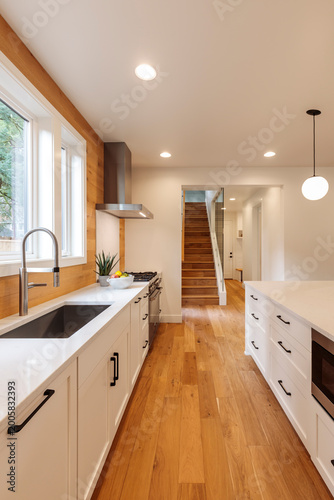 A modern white kitchen with wood floors and minimalist design. Lights on for a lighting option.