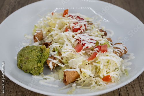Hearty plate of flautas smothered in guacamole, sour cream, and cabbage to satisfy that urge for a Mexican food meal