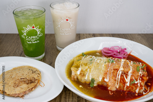 Hearty feast of Mexican food and drink on the table family style consisting of a wet burrito, gordito, and aqua fresca horchata and cucumber water to wash it down