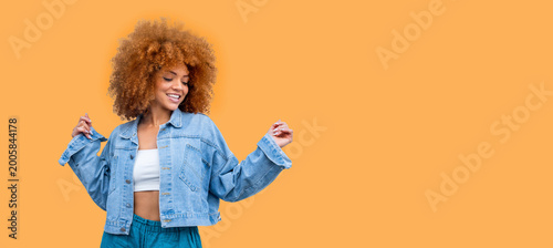 Obraz na płótnie Playful happy young African American woman wear stylish denim clothes dancing and jumping funky black teen fashion girl on orange background