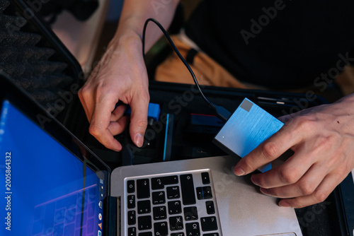 Close-up of hands connecting portable SSD drive to laptop via USB. Technician works on data transfer or backup from inside protective equipment case. Technology workflow concept.