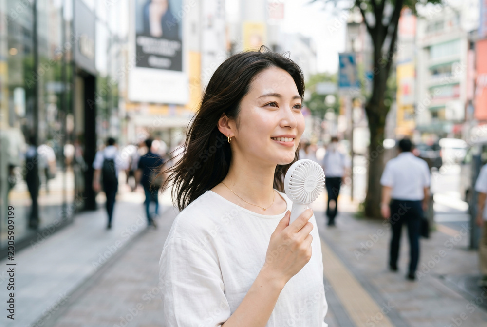 Fototapeta premium ハンディファンを使って暑さ対策をする笑顔の日本人女性、熱中症予防 Generative AI