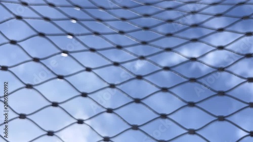 Blue sky and clouds timelapse through metal wire mesh fence with bokeh full frame loop background footage