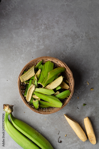overhead view of green plantain peels in a woven basket on a grey countertop, top view of unripe plantain or banana peels in a basket on a textured grey background
