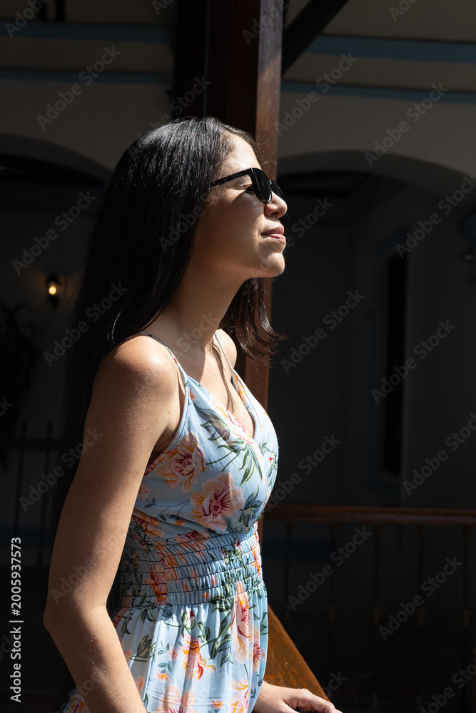 Fototapeta premium Beautiful brunette woman in floral dress posing near colonial architecture with a calm and fashionable appearance.