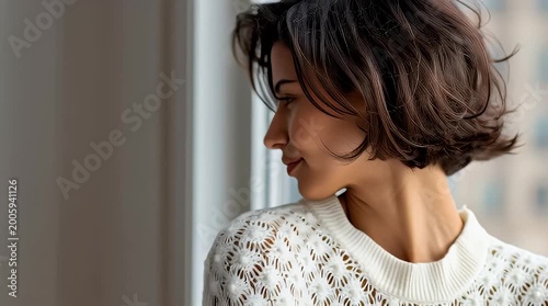 Pensive young woman with stylish bob haircut gazes out a window at a blurred cityscape background conveying introspection and modern elegance for lifestyle marketing