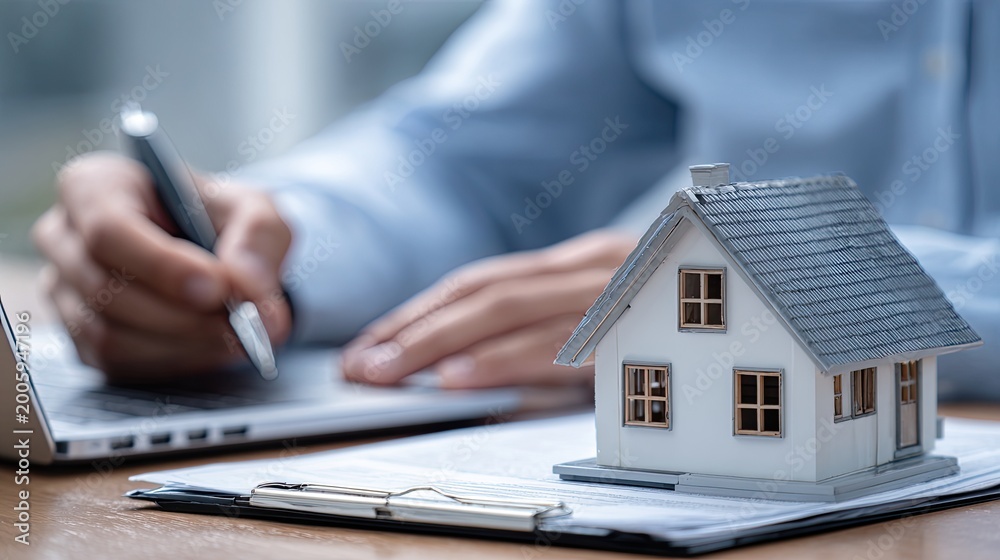 Fototapeta premium Person signing document near miniature house and laptop