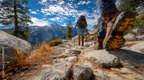 Hikers traverse a rocky mountain trail under a vast, cloudy sky