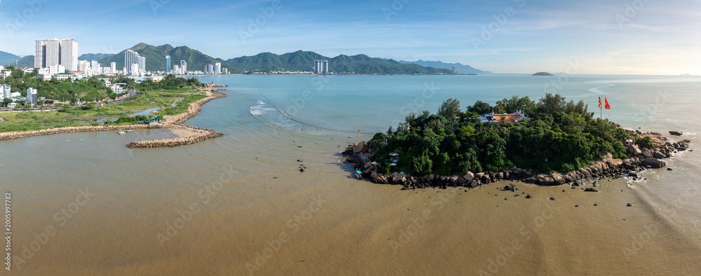 Obraz premium A serene aerial view of Chua Tu Ton temple on a rocky island off the coast of Nha Trang, Vietnam. The Buddhist temple, surrounded by lush greenery, overlooks the calm sea.