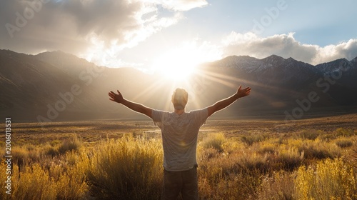 Person arms outstretched to bright sun over golden plains and mountains