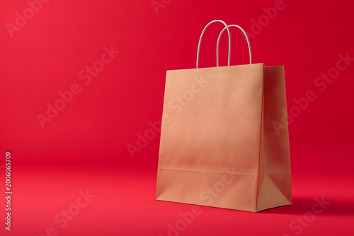 A blank paper shopping bag with a handle is isolated on a red background as an empty retail gift package for merchandise