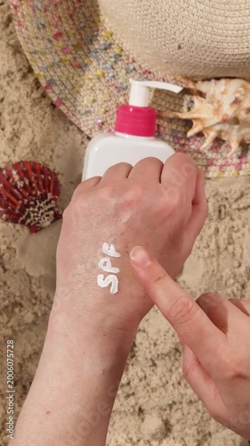 Woman applies white cream labeled spf on her hand on sand by beach. Skincare routine for sun protection against uva and uvb rays on tropical vacation. Preventing photoaging and skin cancer risk.