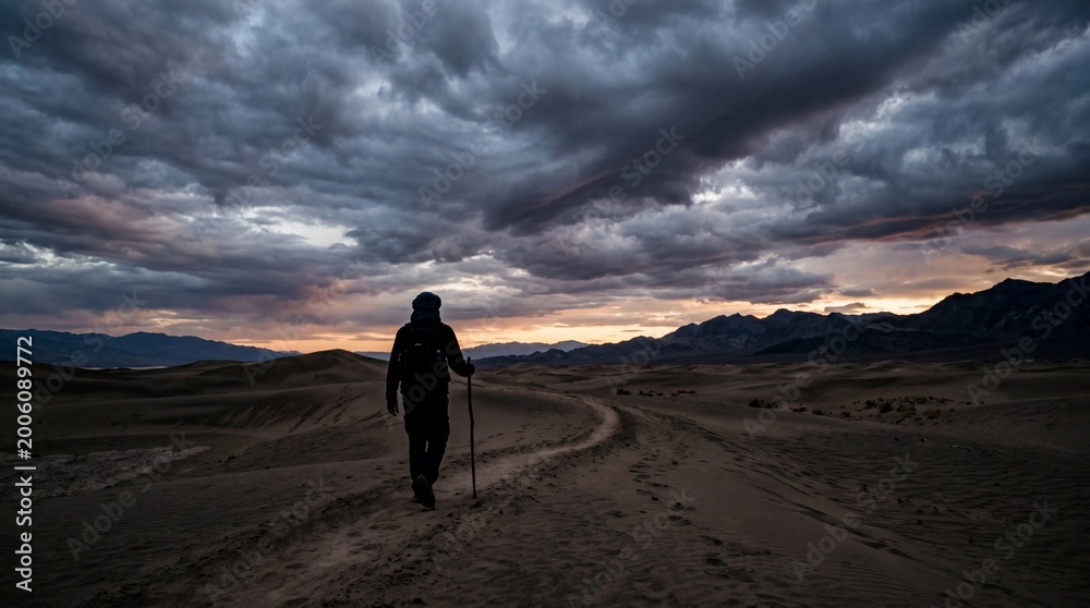 Obraz premium Silhouette of a traveler walking through a desert landscape under a dramatic cloudy sky at dusk