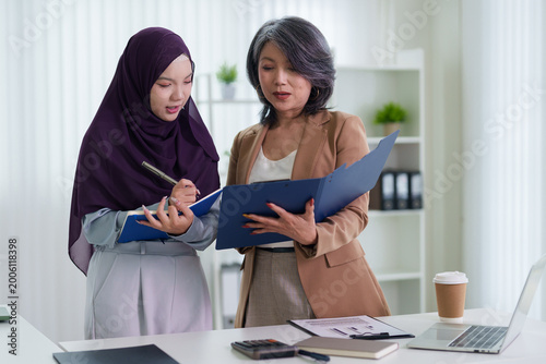 Asian businesswomen colleagues reviewing documents folder together discussing business project report teamwork collaboration modern bright office workplace