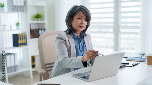 Asian business woman professional working laptop computer office desk analyzing data finance report modern bright workspace corporate employee concentrated