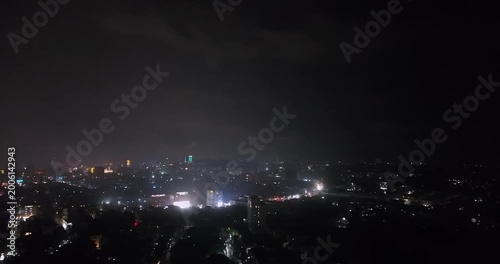 Night aerial view of a city skyline with a dramatic lightning strike illuminating the dark, stormy clouds above the urban lights.