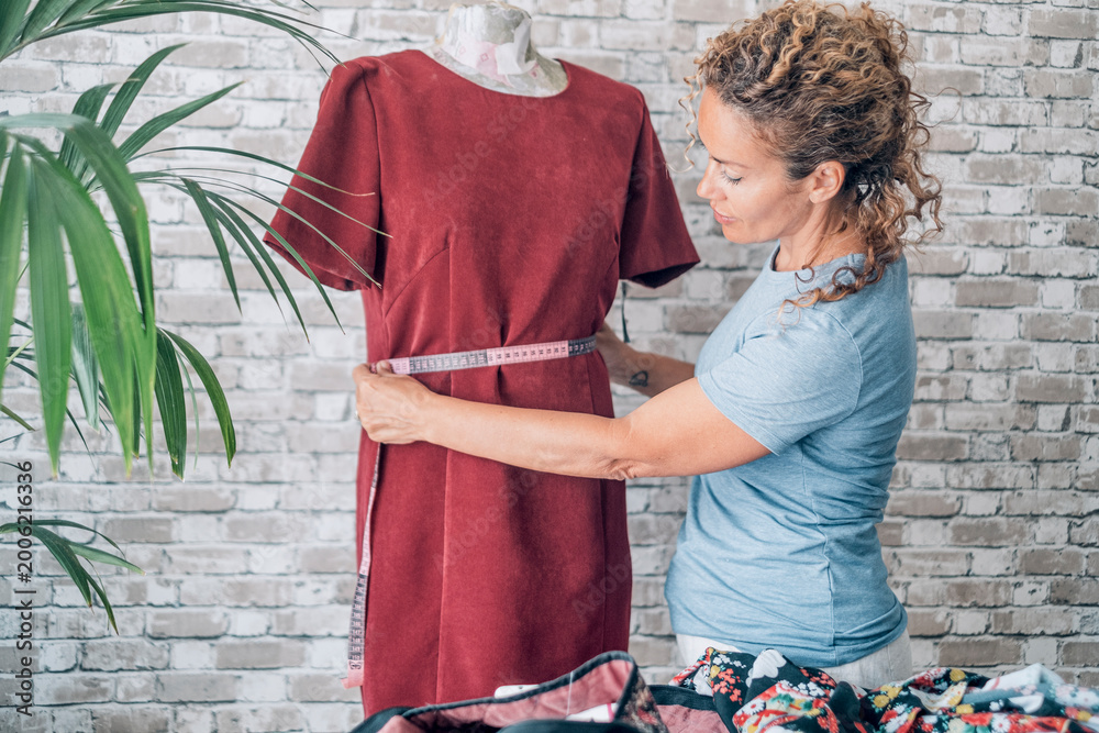 Obraz premium Professional woman fashion designer working in her creative studio, taking measurements of a new red dress on a mannequin while creating a custom design