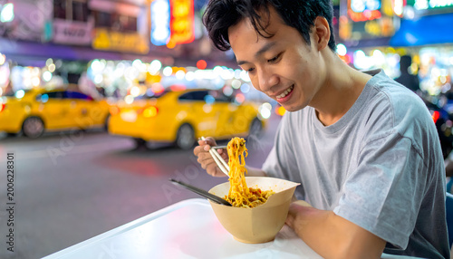 Person sitting at a small plastic table on a neon lit street eating steaming spicy noodles with blurred background traffic generative AI