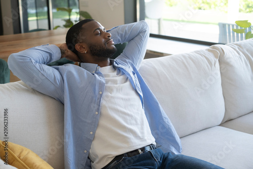 Canvas Print Young man relaxing eyes closed on a comfortable light sofa, enjoying peace, comf