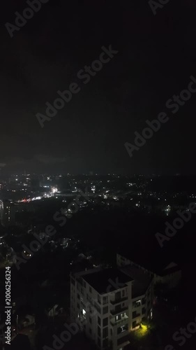 Vertical night aerial view of city lights under dark, stormy clouds with  lightning.