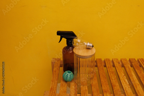 A spray bottle, a glass container, and a small ball are placed on a wooden surface