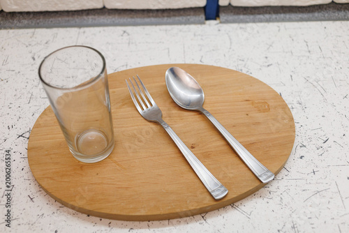 A clear glass sits next to a fork and spoon on a wooden board in a kitchen