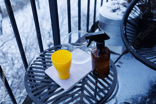 A yellow cup sits next to a spray bottle and clear container on a black table outside in the cold