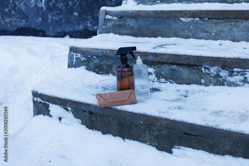 A glass and two bottles rest on steps covered in snow during the winter season