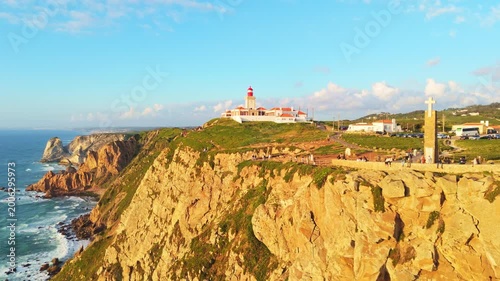 Cabo da Roca, Cliffs and Atlantic Ocean at Sunset. Lighthouse, Cross and Tourists. Portugal. Aerial View. Drone Moves Forward and Upwards