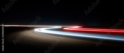 Dramatic long-exposure photograph captures vibrant red white light trails sweeping along dark curving asphalt road.