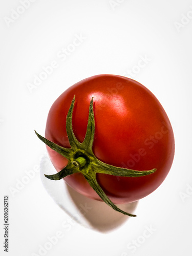  Close-up of a ripe red tomato with a fresh green stem, isolated on a clean white background. Bright, natural lighting highlights the smooth, glossy skin and vibrant color, conveying freshness