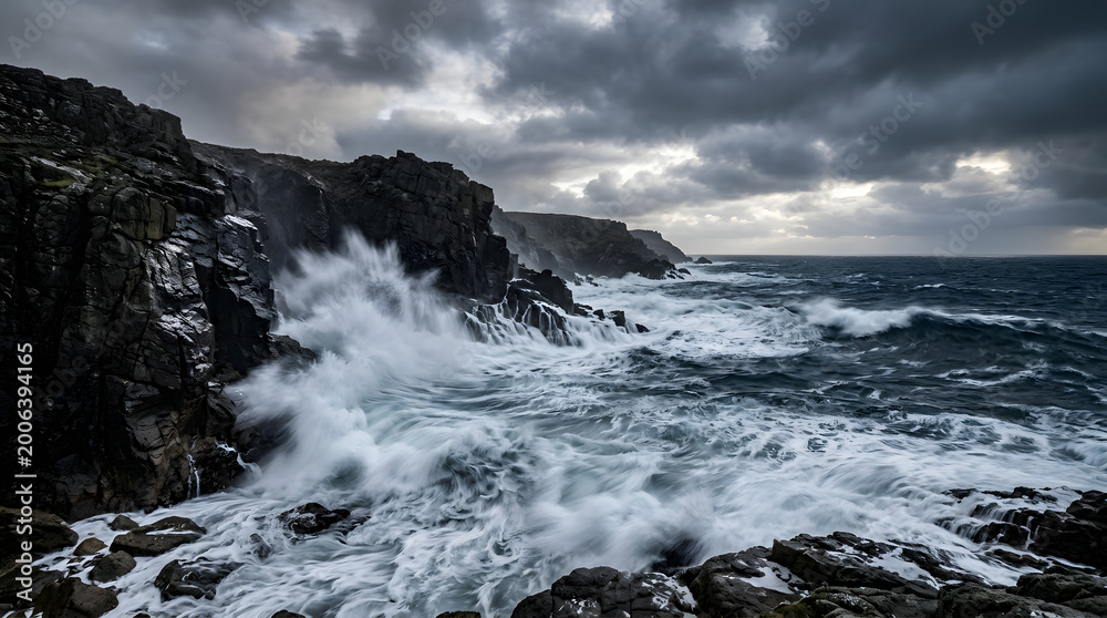 Fototapeta premium A couple walks hand in hand along a rugged coastline with crashing waves and stormy weather.